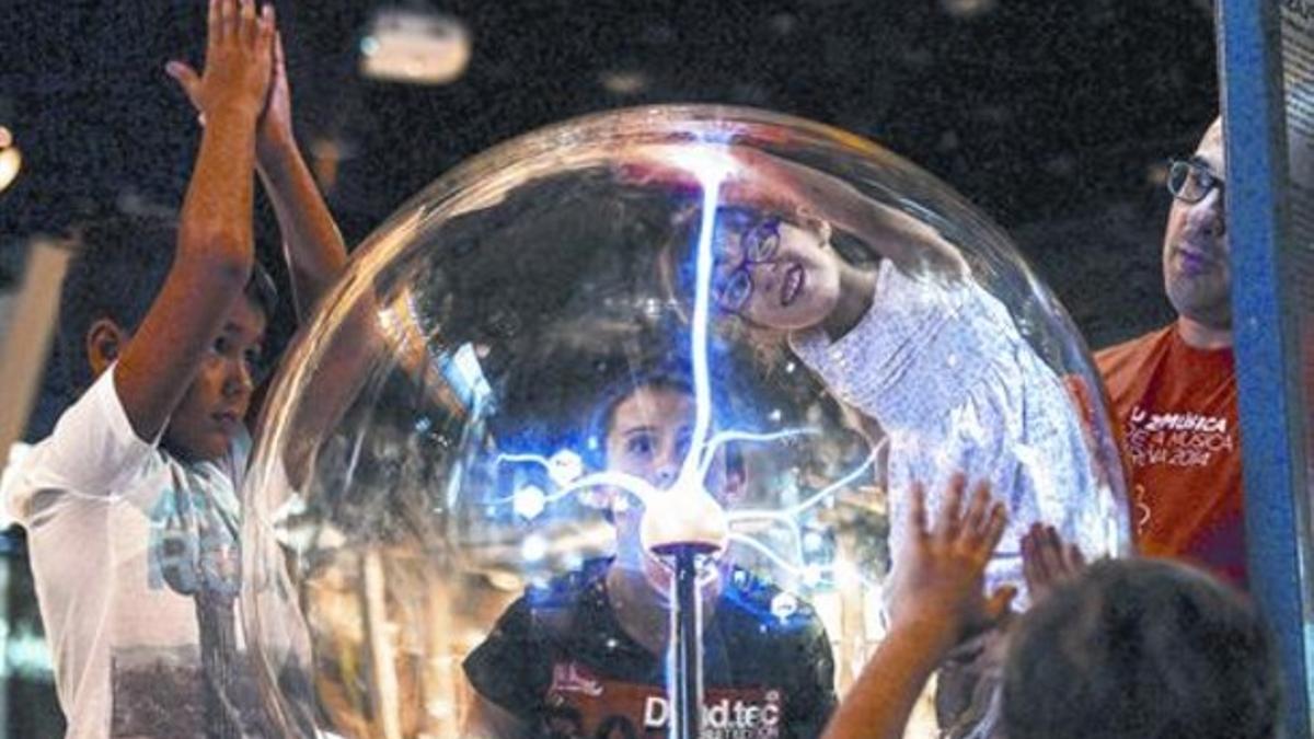 Unos niños experimentan con la la bola de plasma en la zona interactiva de CosmoCaixa.