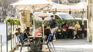 Cantonada dun carrer amb una terrassa en angle, protegida per unes mampares o parets mòbils de vidre, uns para-sols i uns calefactors