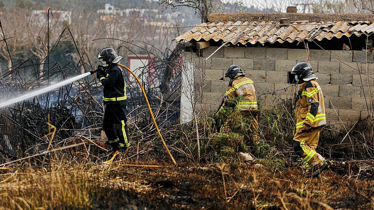 Un bombero y dos brigadistas del Ibanat refrescan la zona del incendio junto a un viejo edificio techado con amianto. 
