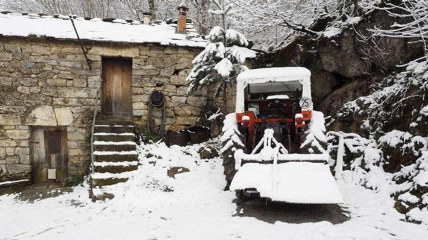 Un tractor cubierto de nieve delante de una casa en As Nogais (Lugo).