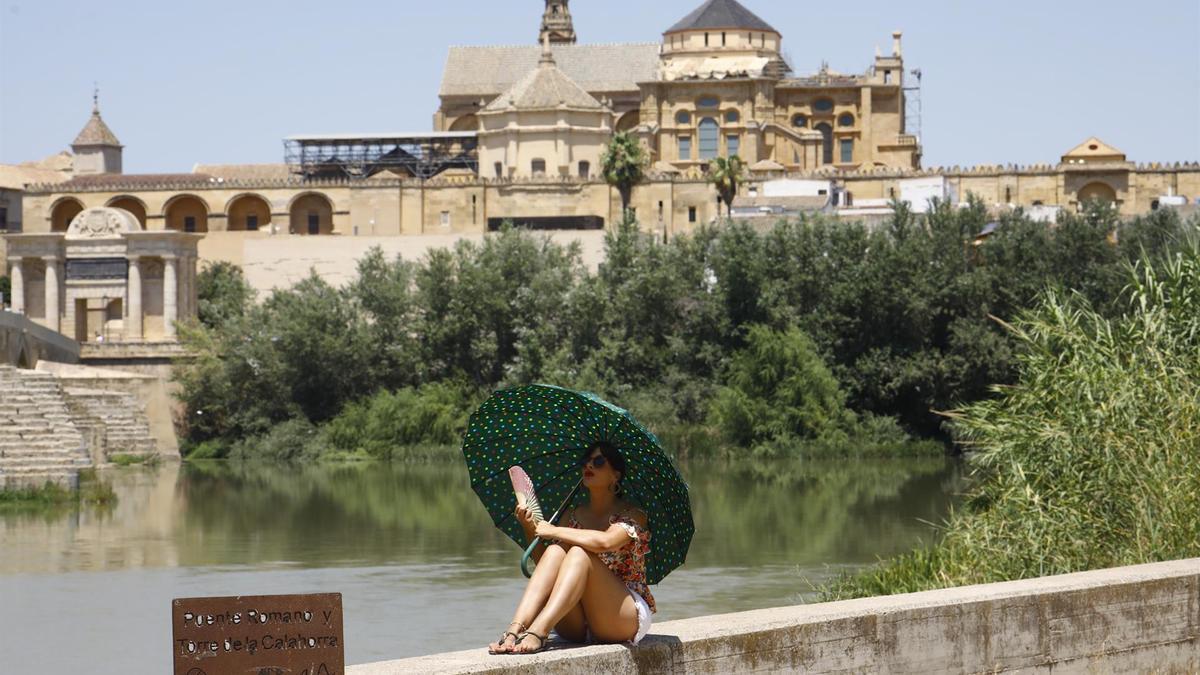 Una turista se protege del calor con un paraguas y un abanico en Córdoba.