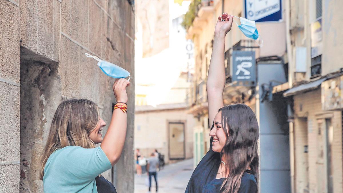 Dos chicas en la parte antigua de Cáceres celebran el fin del uso de la mascarilla.