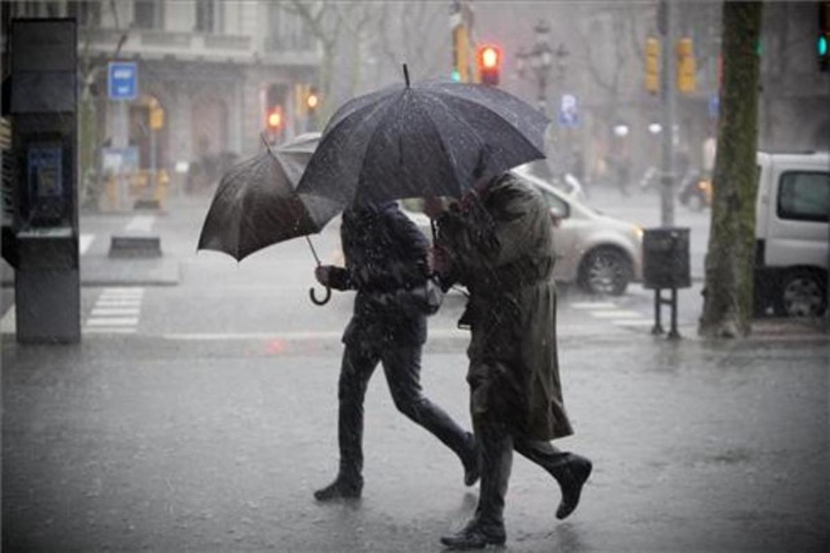 Dos peatones, en Passeig de Gràcia, se protegen del mal tiempo bajo el paraguas en el momento de mayor intensidad de la tormenta.