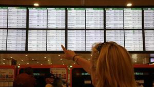 Imagen de archivo de una mujer señalando el panel de información de los trenes de Rodalies de Renfe en la estación de Sants.