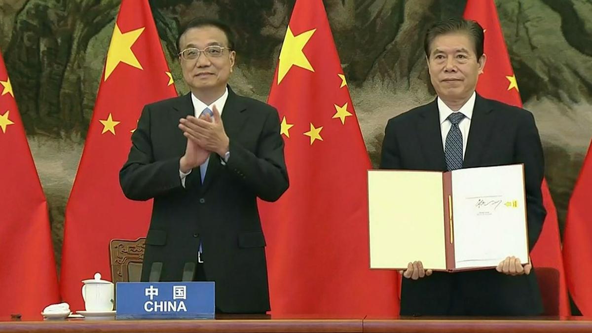 El primer ministro de China, Li Keqiang, aplaude mientras su ministro de Comercio, Zhong Shan, muestra el documento del acuerdo comercial RCEP.