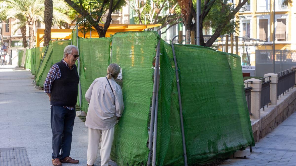 Dos vecinos se asoman por un hueco de las vallas en la plaza Músico Tordera.