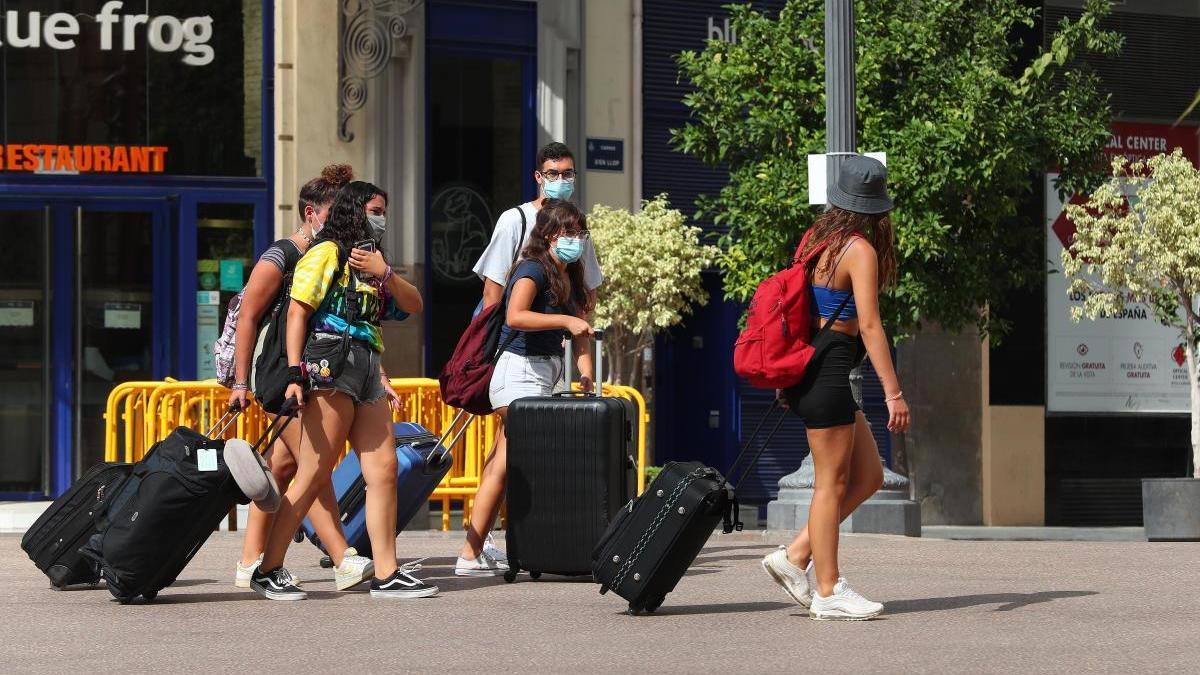 Varias personas, con maletas y mascarillas, por la plaza peatonalizada del Ayuntamiento de València.