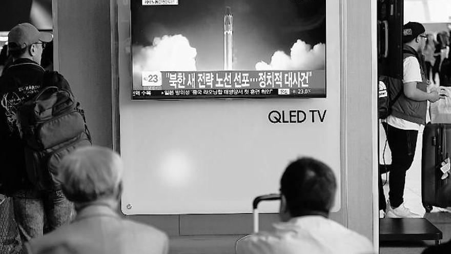 Unos viajeros ven en la pantalla de una estación de tren de Seúl imágenes de archivo del lanzamiento de un misil norcoreano.  // AFP