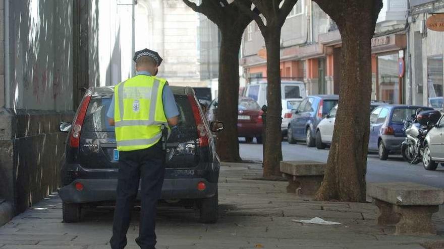 Un policía local multa a un vehículo estacionado en la acera de la calle San Agustín.