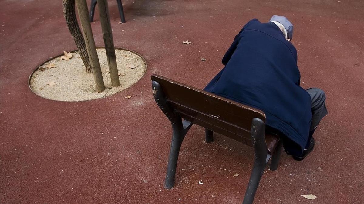 Un anciano, sentado solo en el banco de un parque de Barcelona.