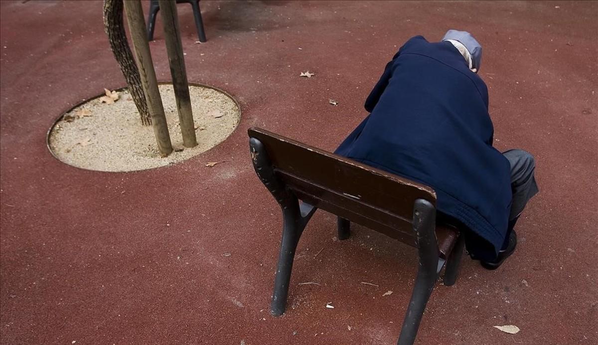 Un anciano, sentado solo en el banco de un parque de Barcelona. 