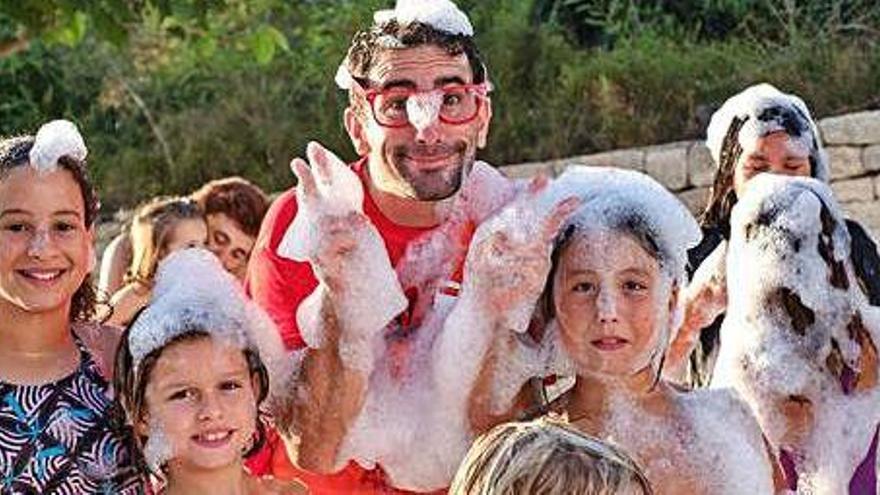 Varios niños jugando con espuma junto al Payaso Cachirulo durante el final de la actuación que llevó a cabo en la plaza de la iglesia de Sant Llorenç.