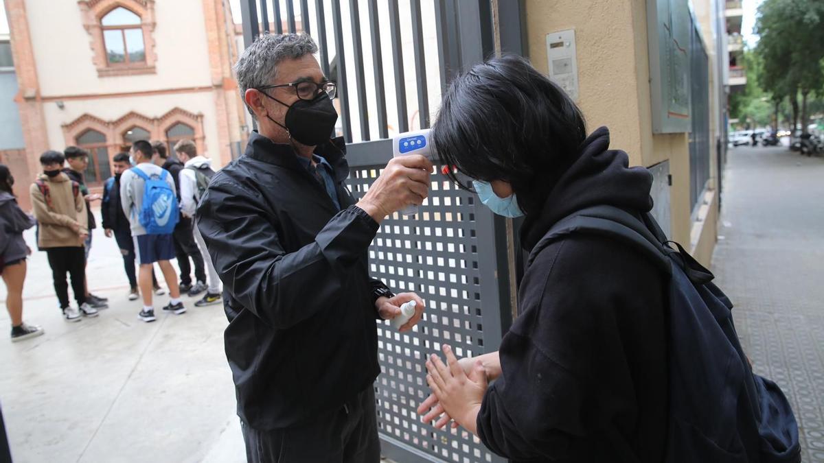 Un profesor de la escuela Mare de Déu del Roser suministra gel hidroalcohólico y toma la temperatura a un alumno.