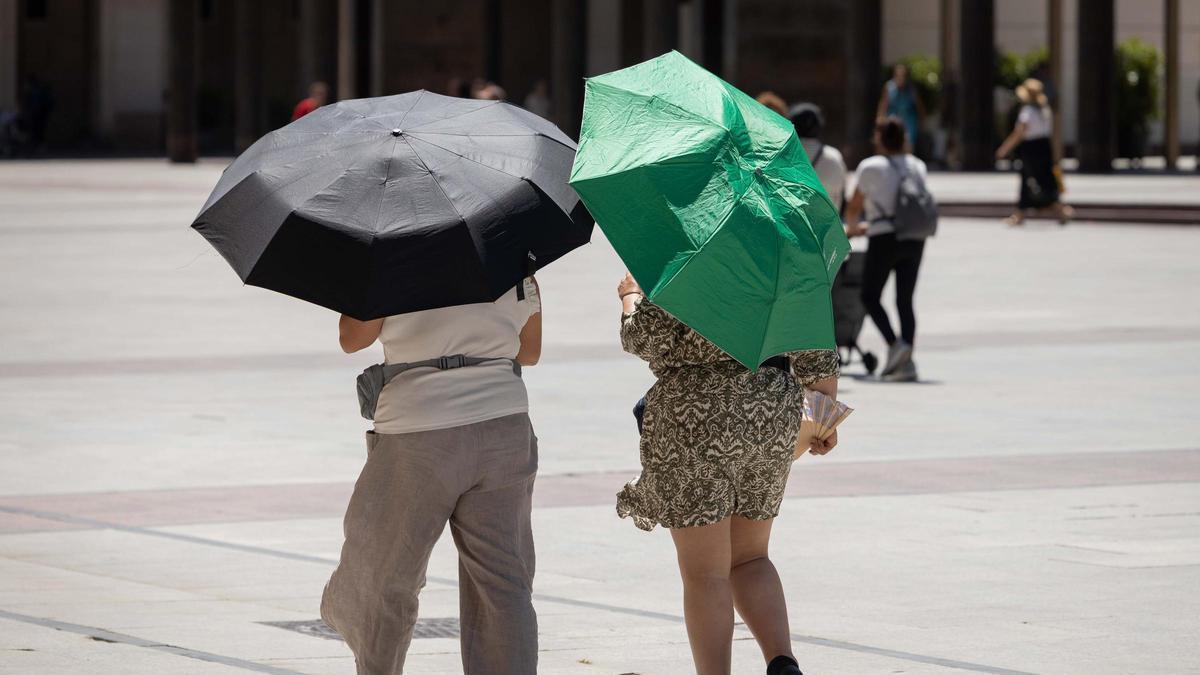 Dos personas se protegen del sol con unos paraguas, en Zaragoza.