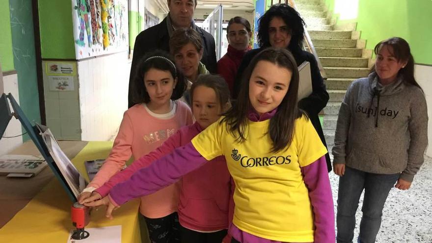 En primer término, las ganadoras Olaya Cardín (delante), Julia Fernández y Alea Lozana (detrás) ponen un matasellos en el colegio de Infiesto. Detrás, Miguel Ángel Coviella, Viri Iglesias, Laura Fresno, Ana Isabel Busto y Aránzazu Machargo.