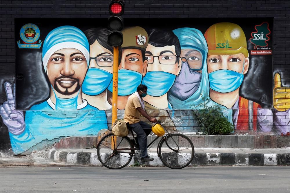 Un hombre pasa en bicicleta por delante de un graffiti en India, en plena crisis por la pandemia del Covid-19. Foto: Reuters