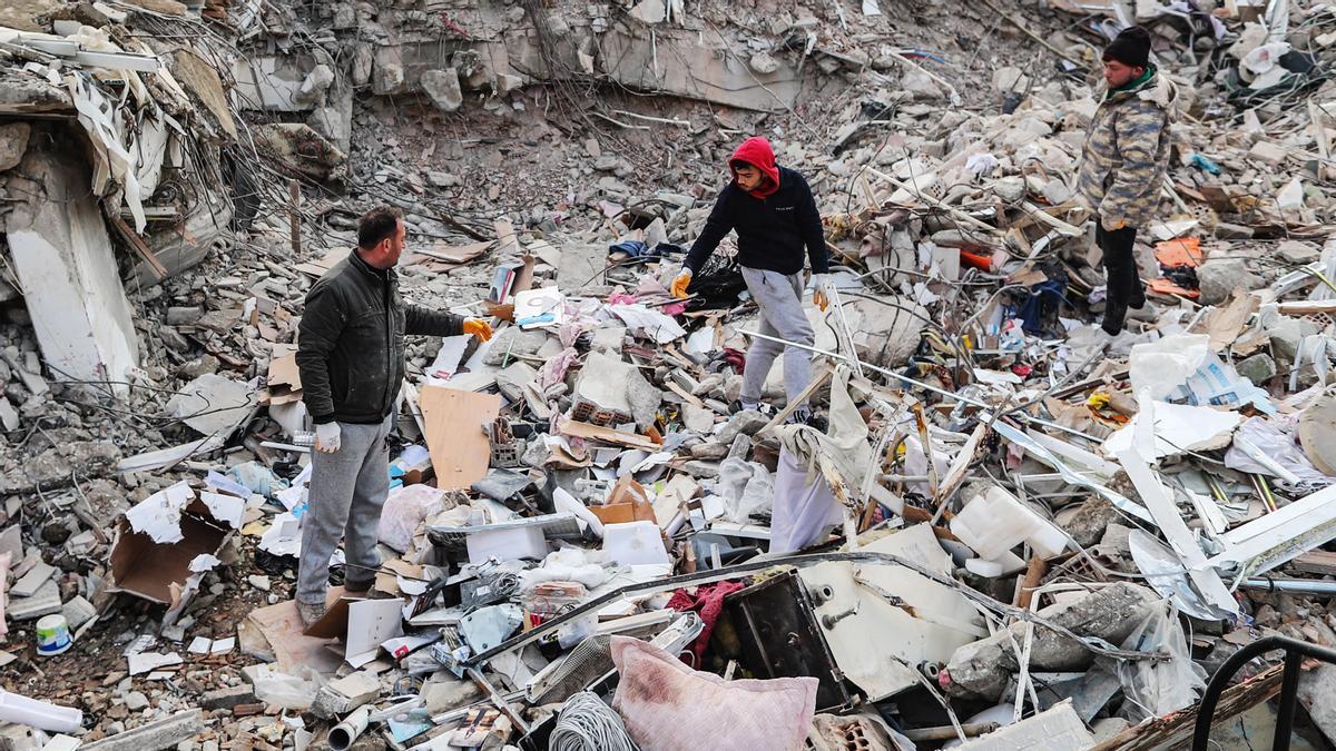 Tres ciudadanos buscan entre los escombros de un edificio derrumbado en la ciudad turca de Hatay