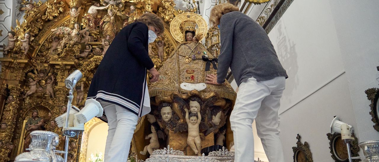 La camarera, Julita Herrera, a la derecha, junto a su camarera auxiliar, Marisa Domínguez, colocan el manto de la ciudad a la Montaña, que luce crespón negro.