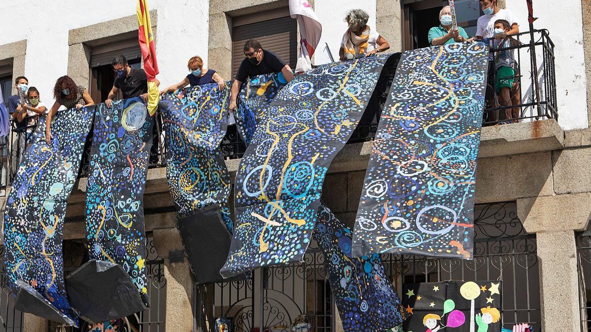 Despliegue del mural colectivo, dirigido por la ilustradora Leticia Ruifernández, desde el balcón del Ayuntamiento de Bermillo. | Ana Burrieza