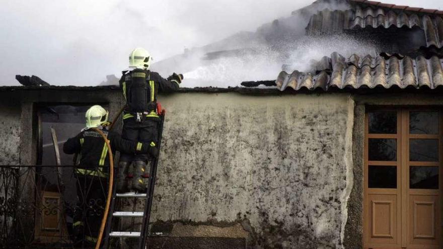 Dos bomberos extinguen las llamas desde el tejado del inmueble. // Bernabé/Luismy