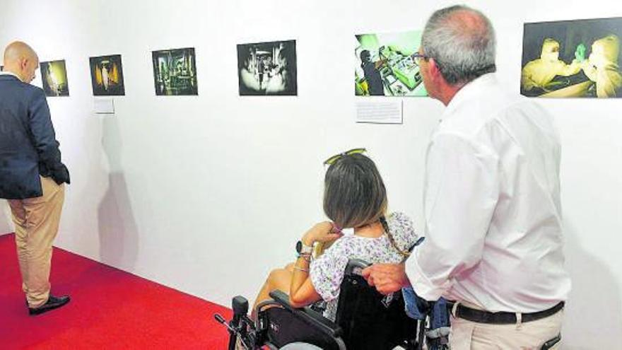 Varias personas contemplan la exposición de fotos homenaje a los auxiliares clínicos. | | JUAN CARLOS CASTRO