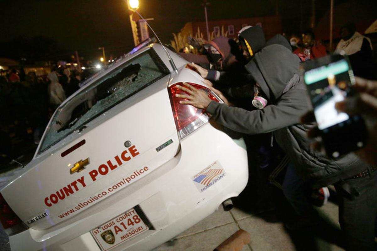 Un grupo de ciudadanos tratan de volcar un coche de la policía, en Ferguson.