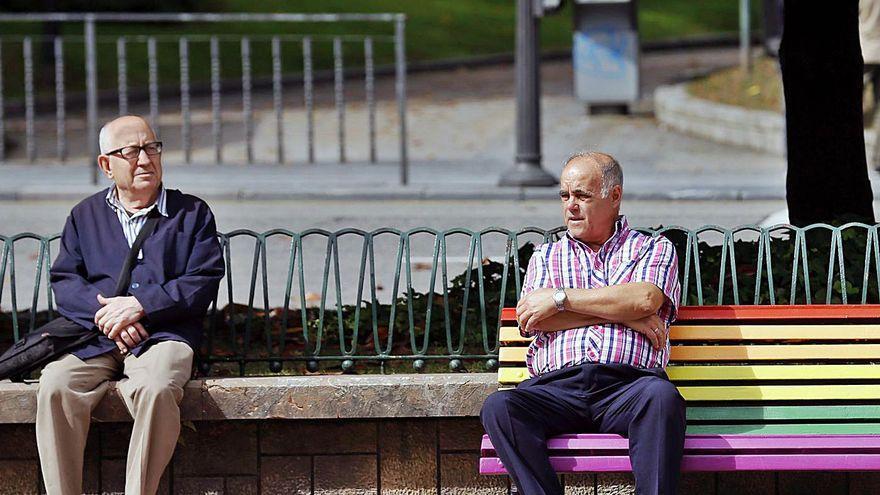 Dos hombre, uno de ellos sentados en un banco con los colores del arcoíris, símbolo del colectivo LGTB.