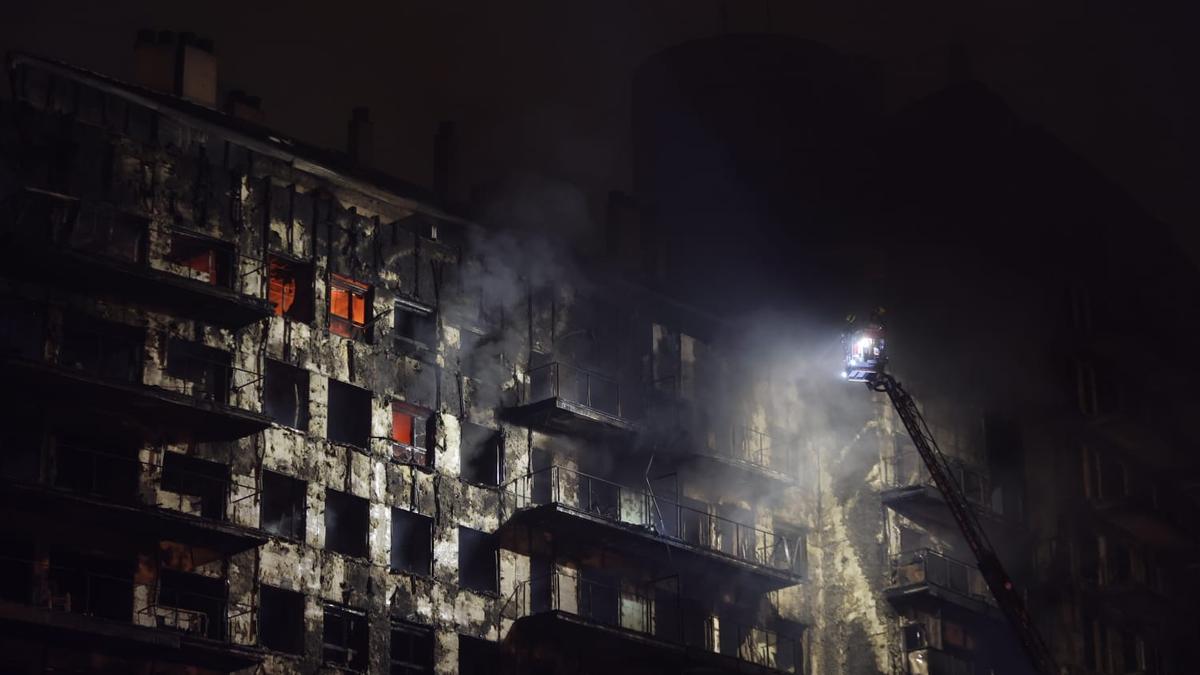 Una grúa lanza agua al edificio calcinado por fuera y todavía con fuego en su interior, ayer por la noche