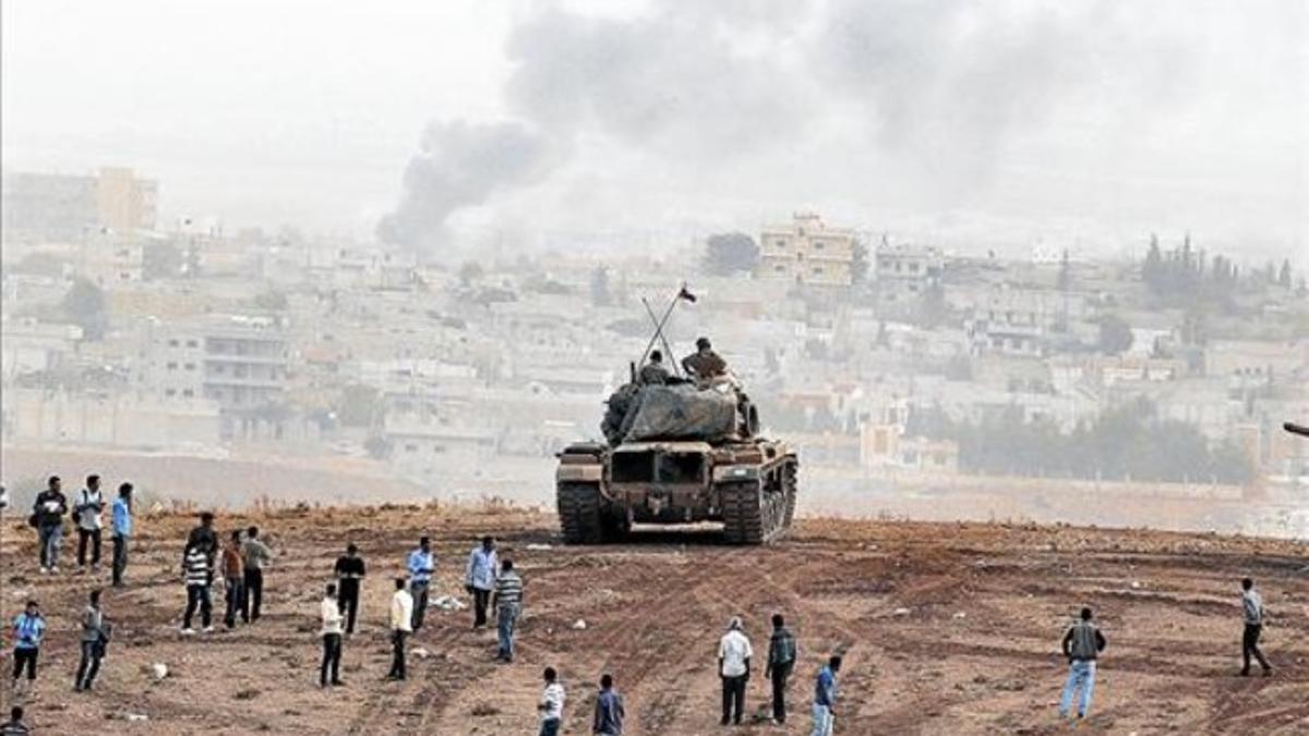 Kurdos de Turquía observan junto a un tanque las columnas de humo que salen de la ciudad siria de Kobani.