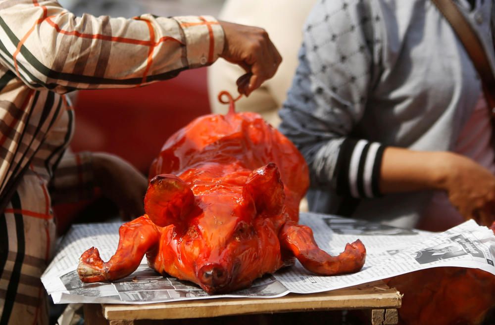 A vendor prepares a grilled pig for sale along a ...