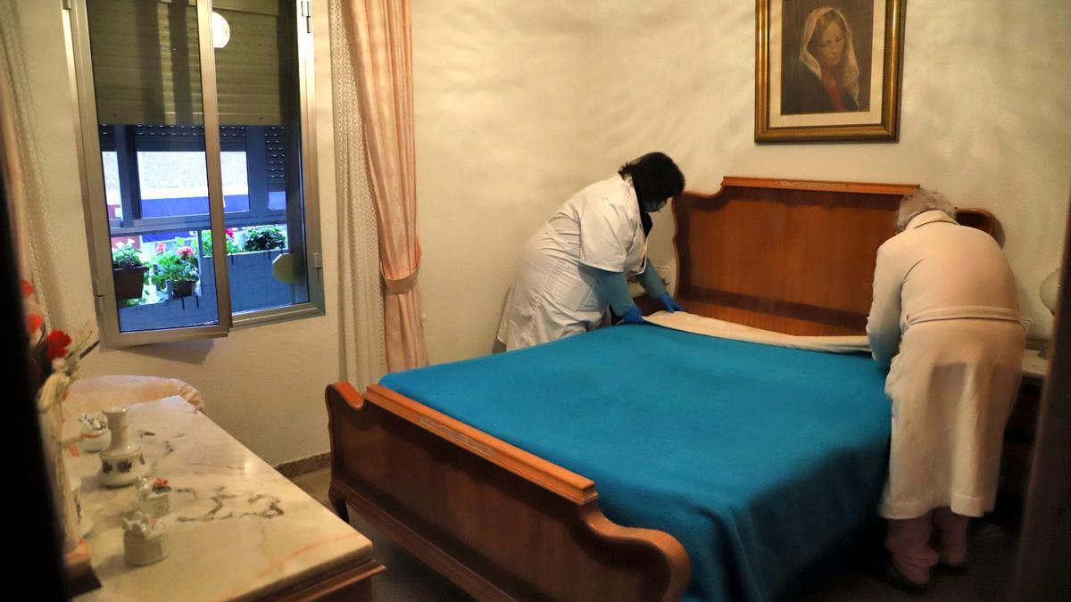 Una cuidadora ayuda a una mujer mayor a estirar las sábanas en una vivienda.