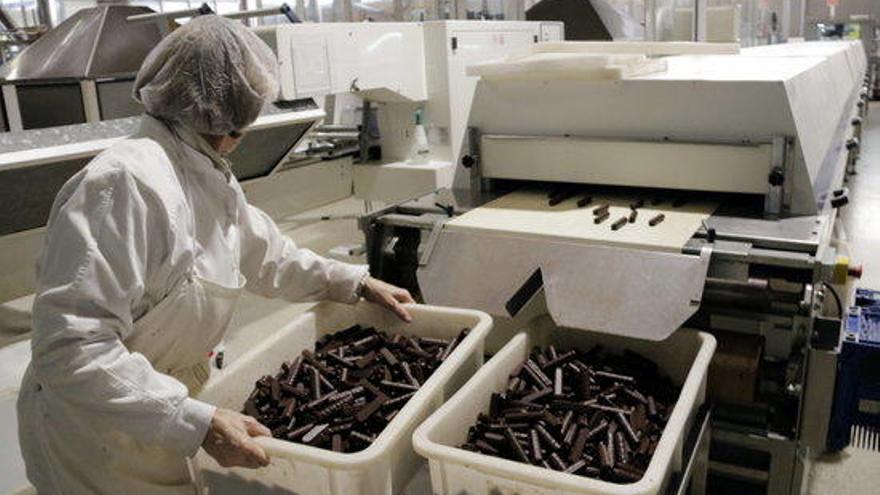 Una treballadora de Galetes Trias agafant neulets banyats amb xocolata i portant-los a la línia de producció que els envasa