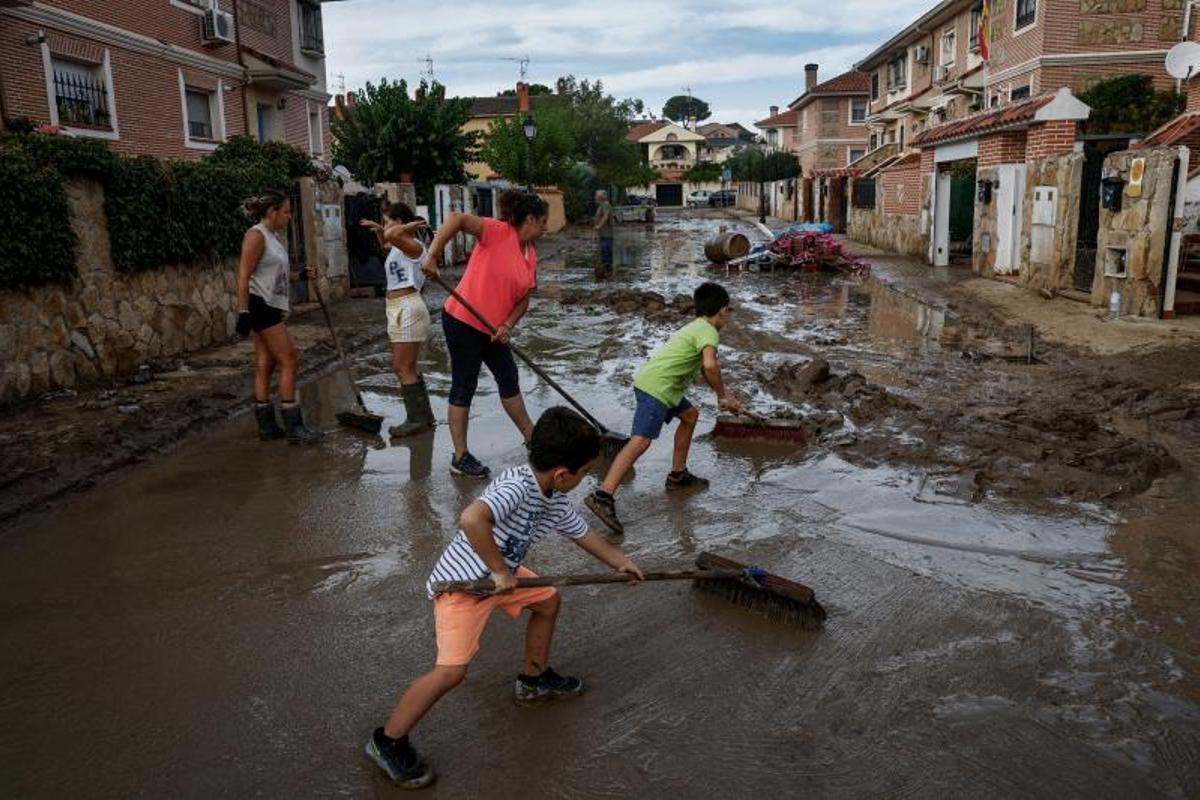 Carmen Palomino y sus hijos Mario, de 8 años, y Alex, de 6, barren el barro mientras ayudan a los vecinos después de las fuertes lluvias en Villamanta, España, el 6 de septiembre de 2023.