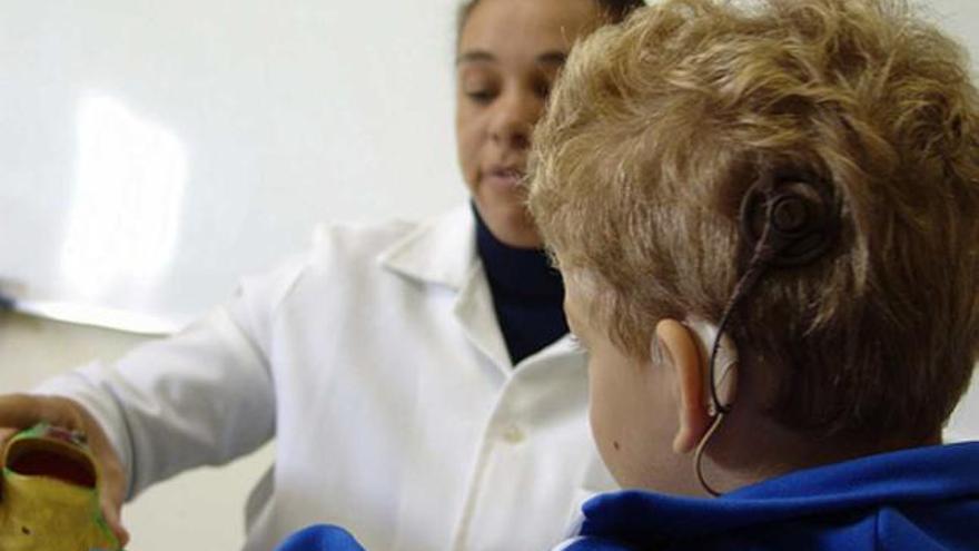 Un menor con un implante coclear presta atención a su educadora.