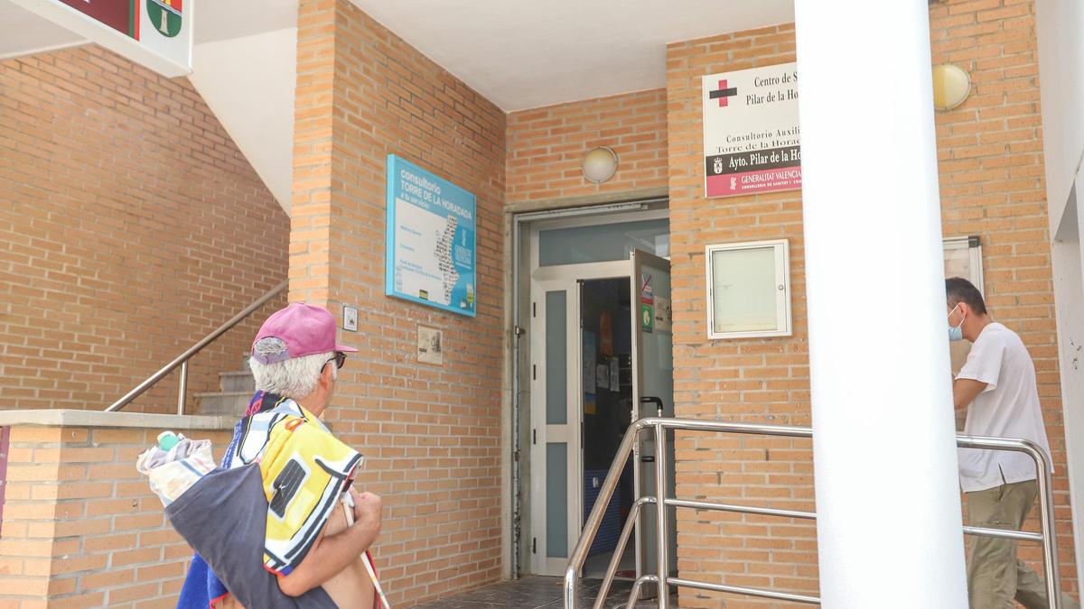 Un hombre con sombrilla y toalla a la puerta del centro de salud de Pilar de la Horadada.
