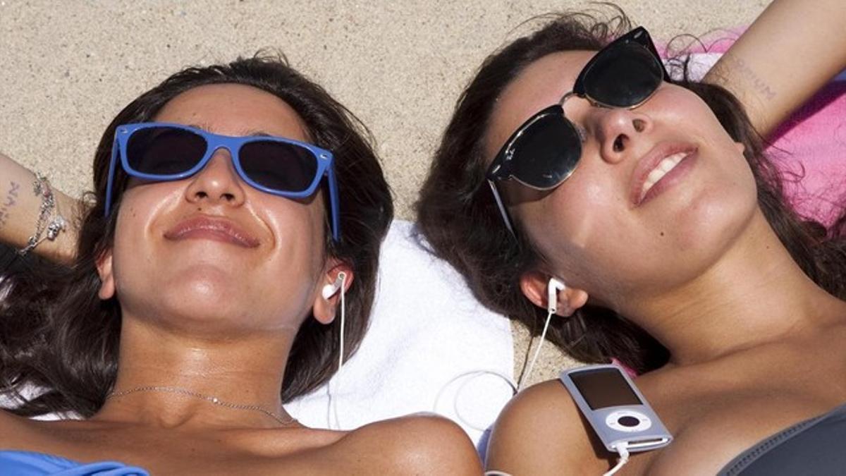 Dos chicas con auriculares en la playa: un reproductor MP3 puede utilizarse tanto para escuchar música como audiolibros.