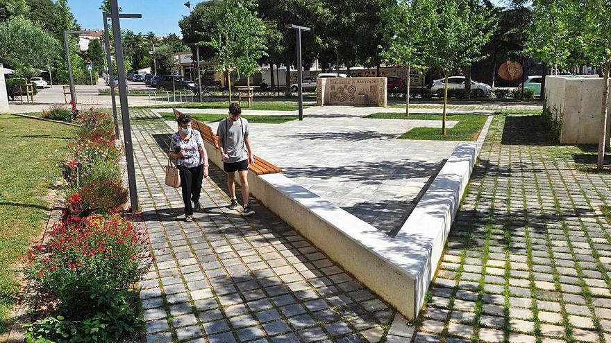 Dues persones travessen la plaça dels pisos de «la Caixa», acabada de millorar.