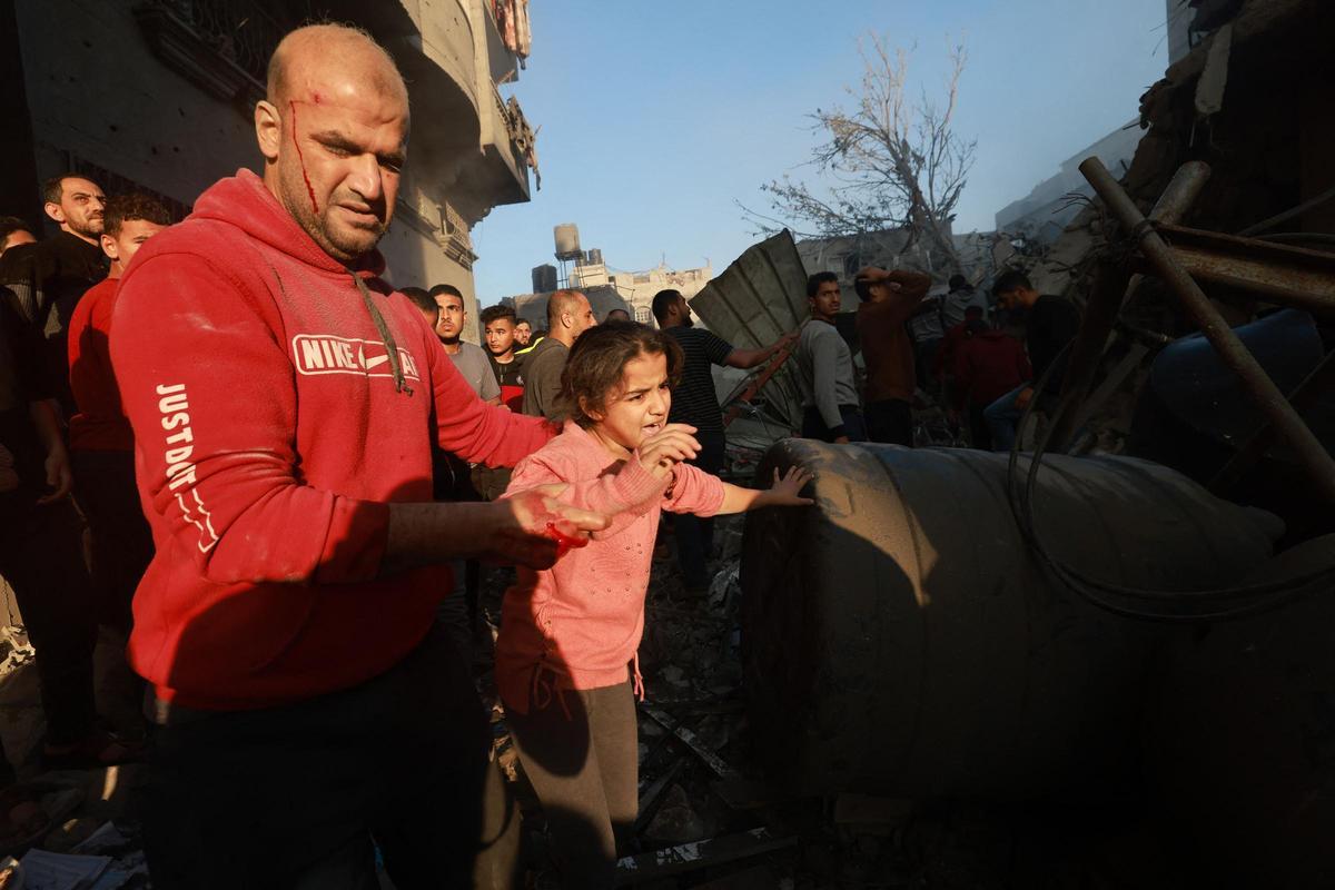 Un palestino herido ayuda a una niña a salir de una zona bombardeada en el campo de refugiados de Rafah, en el sur de la Franja de Gaza, el 1 de diciembre de 2023, mientras los combates se reanudaban poco después de la expiración de una tregua de siete días entre Israel y los militantes de Hamás.