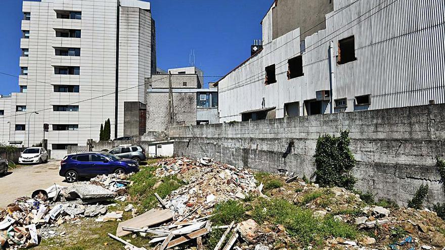 Escombro en un terreno y un edificio abandonado, con el Hospital Montecelo al fondo.