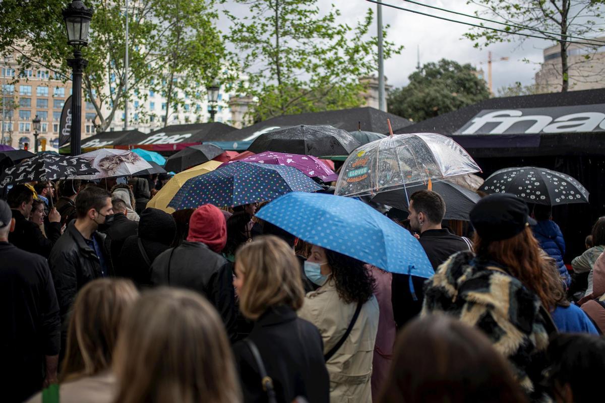 Varias personas, con paraguas, en la feria literaria de Sant Jordi, en el día Internacional del Libro, a 23 de abril de 2022, en Barcelona