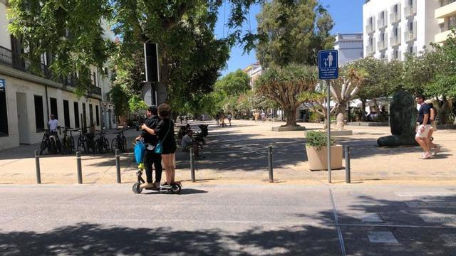 Dos usuarios en un patinete eléctrico con la señal de prohibición a la derecha. | FOTOS: A.B.P