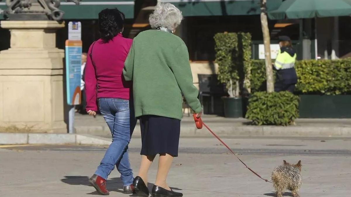Una mujer mayor pasea con su cuidadora por una calle de Barcelona.