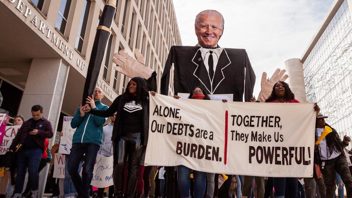 Manifestantes marchan con una pancarta y un cartel de Biden alrededor del Departamento de Educación durante una manifestación para pedir la condonación de deudas universitarias.