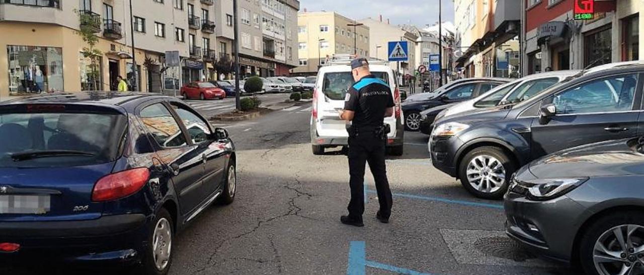 Un agente de la Policía Local de Cambre multa a coches en doble fila, este mes, en O Temple.