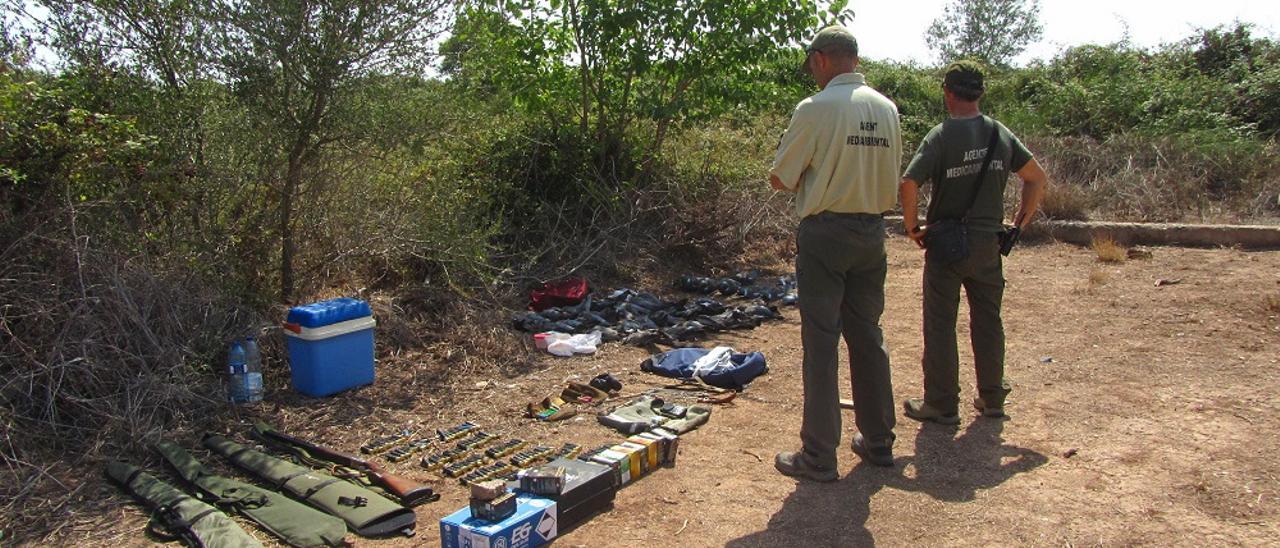 Los dos agentes medioambientales miran las armas y la munición incautadas