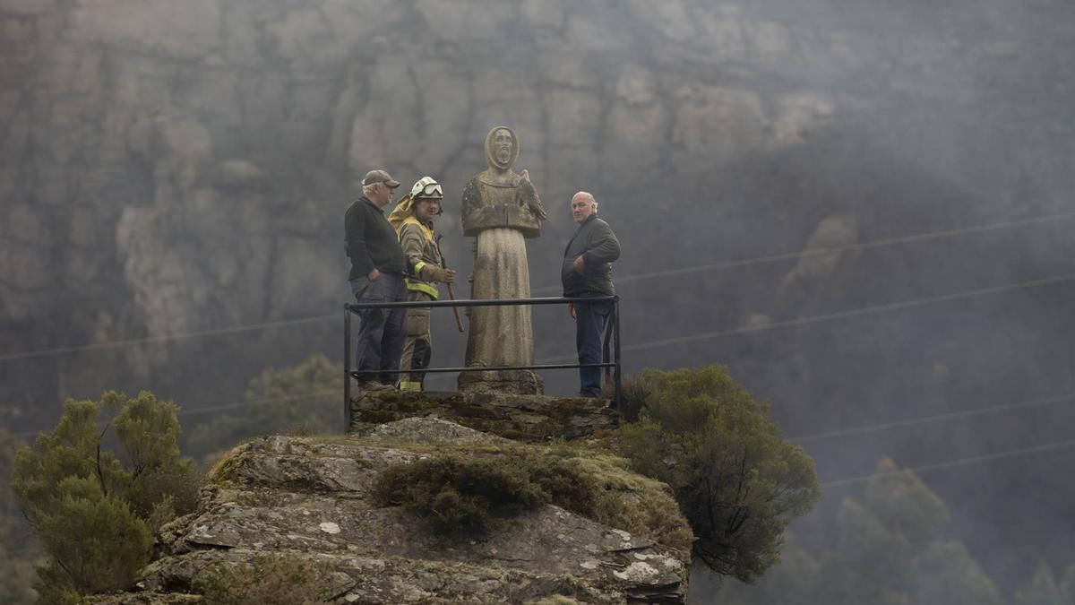 Dos hombres y un guarda forestal observan el monte quemado por el incendio forestal de Baleira