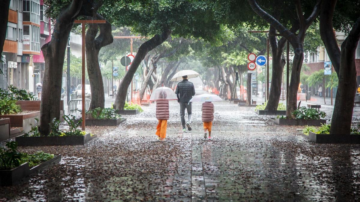 Personas se cubren de la lluvia con un paraguas mientras caminan por una vía.