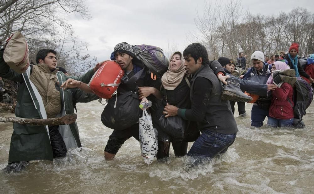 Dos refugiats ajuden a una dona a creuar un riu en la seva ruta a Macedònia