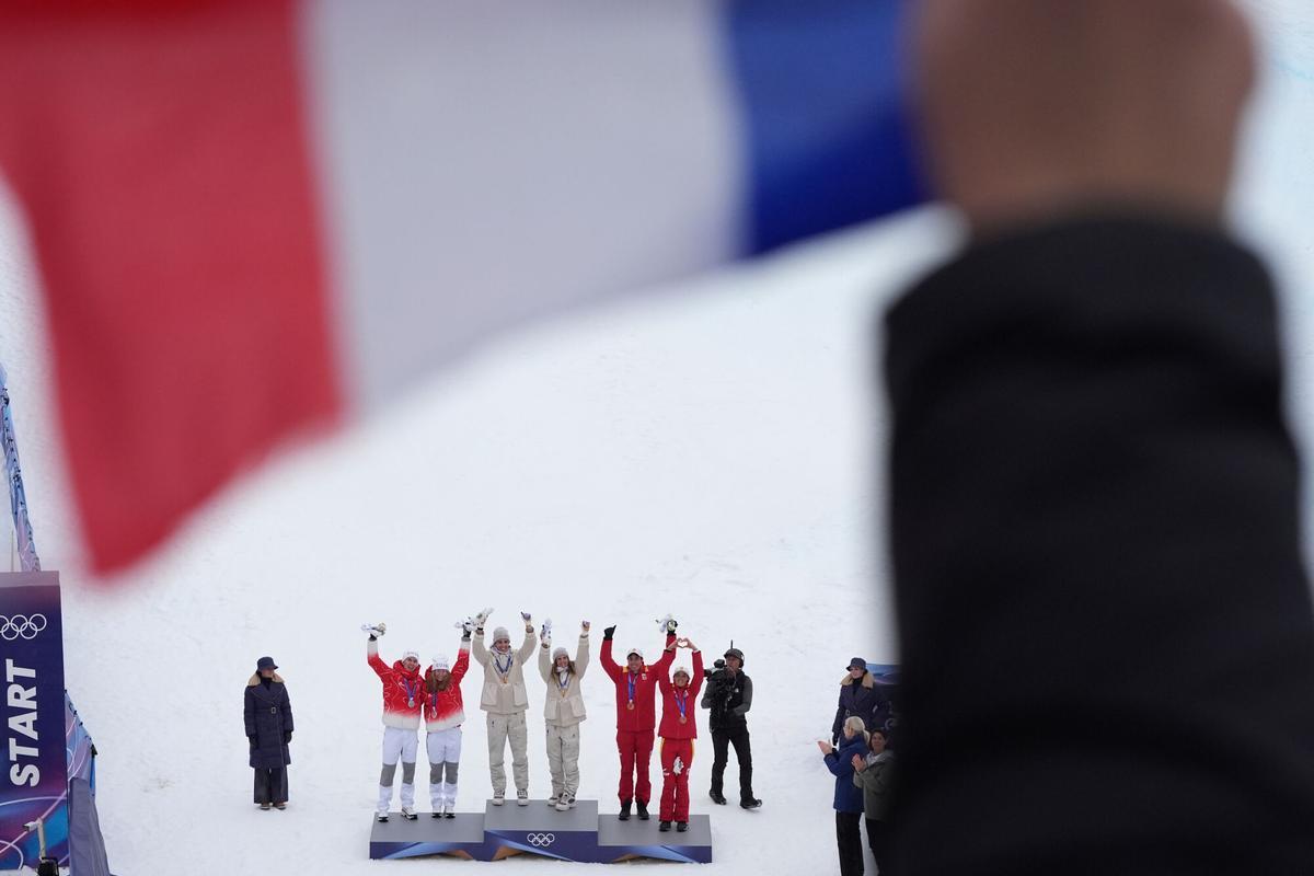 Fans wave a French flag as gold medalists France's Thibault Anselmet and Emily Harrop, center, stand next to silver medalists Switzerland's Jon Kistler, left, and Marianne Fatton and bronze medalists Spain's Oriol Cardona Coll, and Ana Alonso Rodriguez, right, for a ski mountaineering mixed relay, at the 2026 Winter Olympics, in Bormio, Italy, Saturday, Feb. 21, 2026. (AP Photo/Rebecca Blackwell)