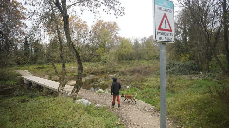 Un noi i el seu gos a punt de travessar l’Onyar pel passallís malmès amb el senyal que adverteix que s’ha d’anar amb precaució. | MARC MARTÍ
